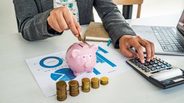 Başarılı bir iş adamı ofiste çalışırken sikkeleri kumbaraya koyuyor. Para biriktirmek gelecek için bir yatırımdır. Banka yatırımı. 