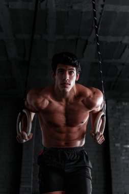 Formda olmayan bir spor salonunda yüzükle yüzen genç ve kaslı bir sporcuyu yakından çek. Profesyonel beden eğitimi sporcusu.