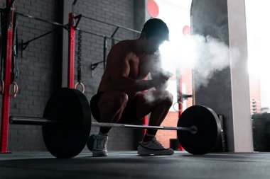 Formda olmayan bir spor salonunda kaldırma hareketine hazırlanan genç üstsüz kas sporcusu. Profesyonel beden eğitimi sporcusu.