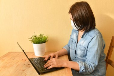 Maskeli kadın bilgisayarda minimalist bir iç mekanda çalışıyor..