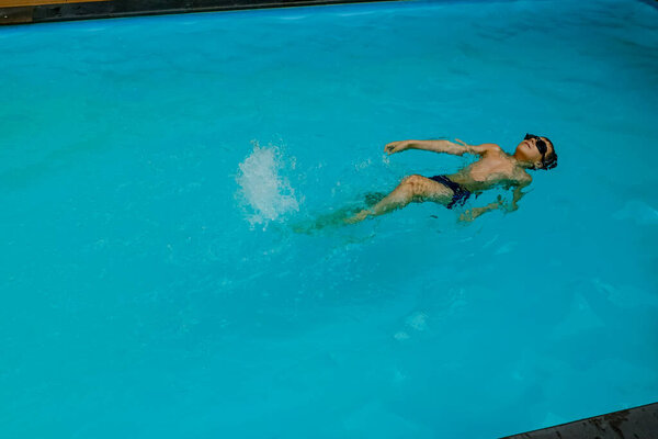 Young boy is swimming on his back in the swimming pool. sport vacation.