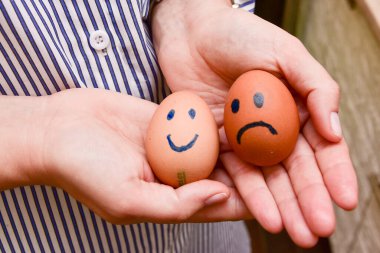 Kadın ellerinde boyalı duygular olan iki yumurta. Gülümseyen ve üzgün yumurtalar.