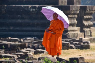 Siem Reap, Kamboçya - 15 Ocak 2019 - Angkor Wat 'ta elinde bir tablet ve şemsiyeyle dolaşan Budist keşiş.