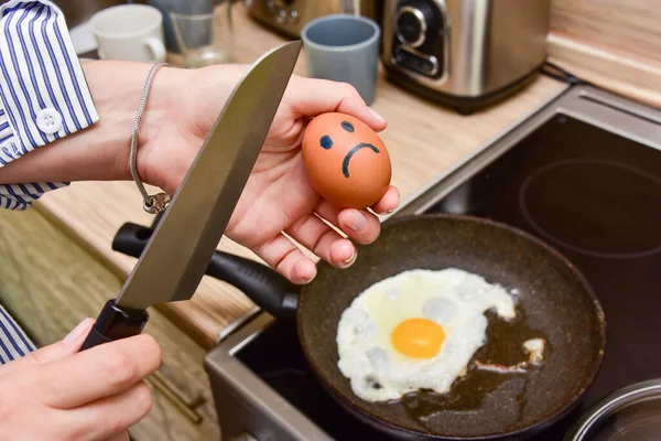 Mutfakta, tavanın önünde duran kadın elinde bir bıçak tutuyor ve gülümseyen üzgün bir yumurta kırıyor..