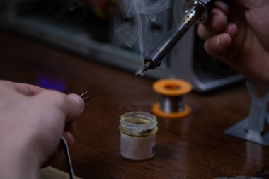 Bir adam kaynak makinesiyle çalışır, elektroniği tamir eder.