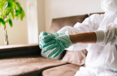 Una mujer con traje de seguridad se quita unos guantes de latex para evitar contagios de una pandemia