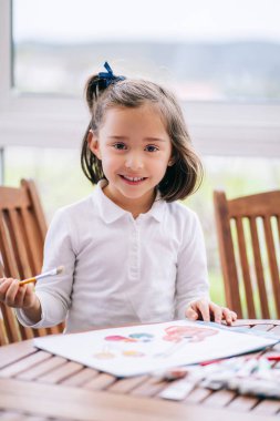 Bir kız suluboya boya ile bazı çizimler yapıyor.