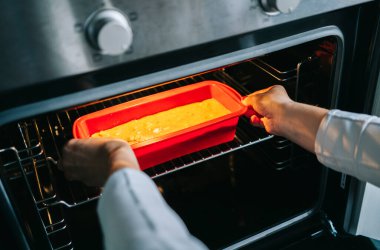 Bir kadın fırına kek koyar.