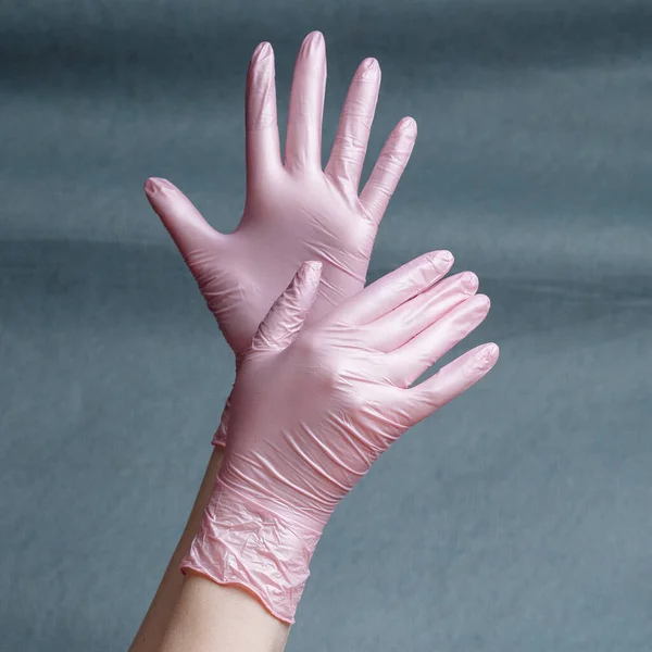Hands in pink nitrile gloves on a gray background with a gradient. Square aspect ratio