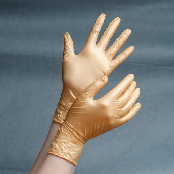 手在灰色背景的灰色梯度上戴着金黄色的氮化手套 正方形比率 — 图库照片