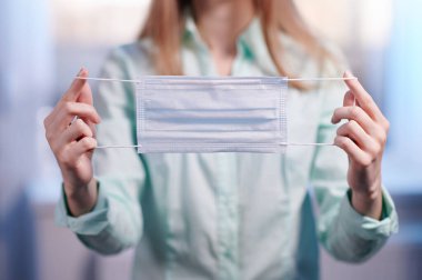 Kızın elinde tıbbi bir maske var.