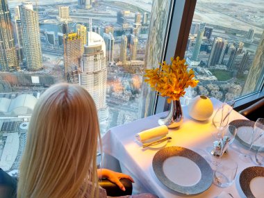 Bir restoranda kahvaltı için bekleyen sarışın pencereden dışarı, muhteşem Dubai 'ye bakıyor..