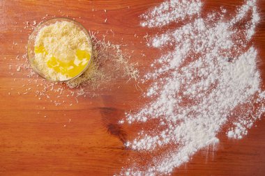 Tabakta yumurta ve ahşap masaya un serpiştirilmiş rendelenmiş peynir.