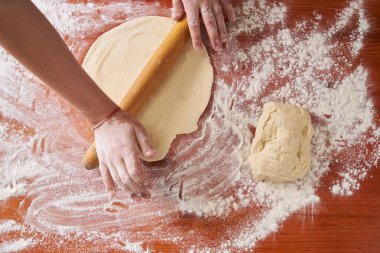 Genç aşçı ahşap mutfak masasında un kaplı sallanan sandalye manzaralı güzel bir hamuru yuvarlıyor.