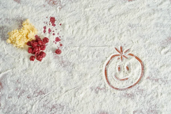 Painted funny smiley in flour on the kitchen table with delicious cherries lying next to them top view