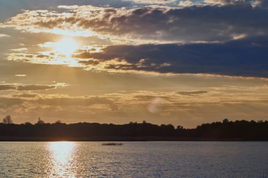 Önünde mavi gökyüzü ağaçları ve su olan güzel bir gün batımı