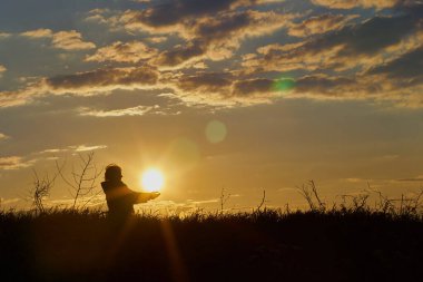 Kız gün batımını ön plandaki güzel mavi gökyüzüne ve çimenlere karşı arka plandaki palmiyelerin içinde tutuyor.