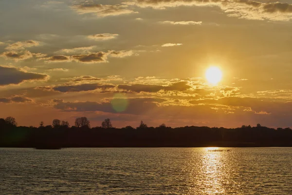 Önünde mavi gökyüzü ağaçları ve su olan güzel bir gün batımı