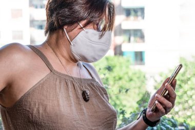 Elinde yüz maskesi olan, cadde arkası olan bir kadının elindeki akıllı telefon. Barselona, İspanya.