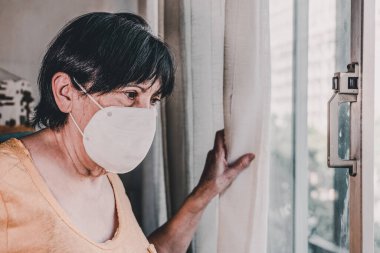 Yaşlı kadın maskesiyle pencereden bakıyor. Barselona, İspanya.