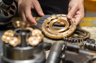 Profesyonel tamirci hidrolik piston pompasının kapak plakasını kontrol etmek ve ağır makineleri tamir etmek için tutuyor. 