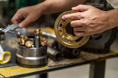 Profesyonel tamirci hidrolik piston pompasının kapak plakasını kontrol etmek ve ağır makineleri tamir etmek için tutuyor. 