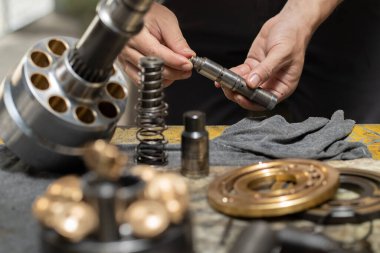 Profesyonel tamirci hidrolik piston pompasının valf çubuğunu kontrol etmek ve ağır makineleri tamir etmek için tutuyor. 
