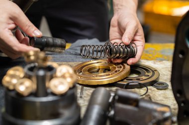 Profesyonel tamirci hidrolik piston pompasının yay vanasını kontrol ve onarım için tutuyor. 