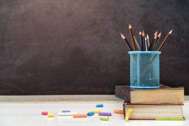 Okula ve eğitim konseptine geri dönmek. Beyaz masa üzerinde kalem tutacağı olan kitaplar. arkaplanda karatahta. 