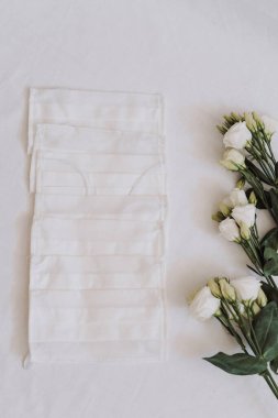 Beyaz bir masada tıbbi maskeler ve beyaz çiçekler.