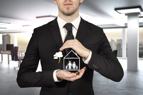 Businessman in office protecting family standing in miniature ho — Stock Photo, Image