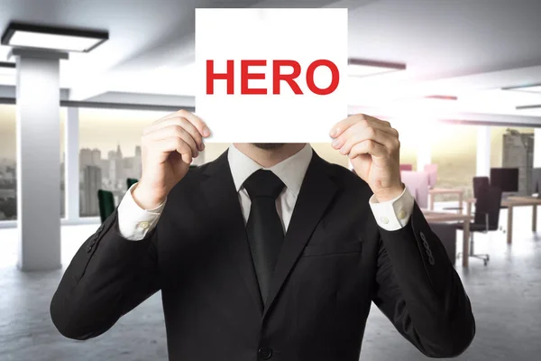 Affärsman i stort kontor gömmer ansiktet bakom skylten hjälte — Stockfoto