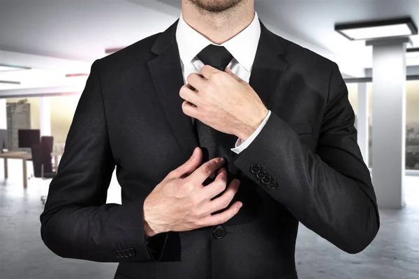 Businessman ties his black tie in modern office — Stock Photo, Image