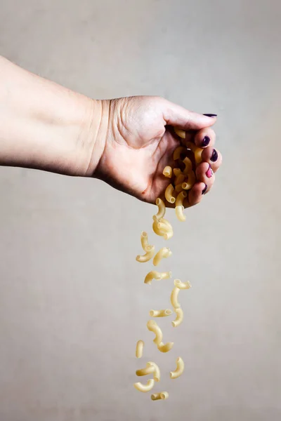 Makarna gri arka planda elden dökülüyor.