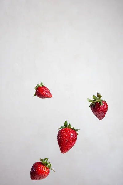 Gri arka planda havada uçuşan kırmızı çilekler.