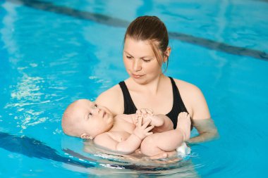 Anne küçük bebeğe su havuzunda yüzmeyi öğretiyor. Çocuklar için yüzme dersleri. Sağlıklı Aile Hayatı.