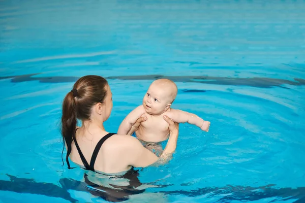Mother teaching happy little baby to swim in water pool. Swimming lessons for children. Healthy Family Life.
