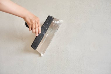 Spatula elinde macunla bir ışık duvarına yaslanmış. İşçi sıva koyuyor. Tamir işleri. Alçılama duvarı.