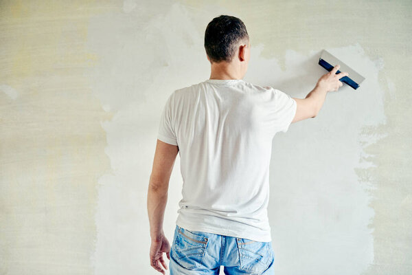 Man plastering the walls with finishing putty in the room with putty knife or spatula. Repair work, decoration building concept, construction.