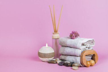Spa malzemeleri, aroma çubukları taşlar, havlular ve pembe arka planda bir bitki.