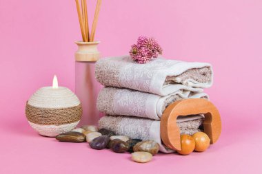 Spa malzemeleri, aroma çubukları taşlar, havlular ve pembe arka planda bir bitki.