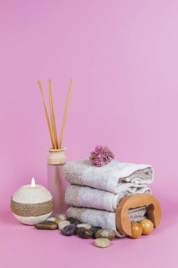 Spa malzemeleri, aroma çubukları taşlar, havlular ve pembe arka planda bir bitki.