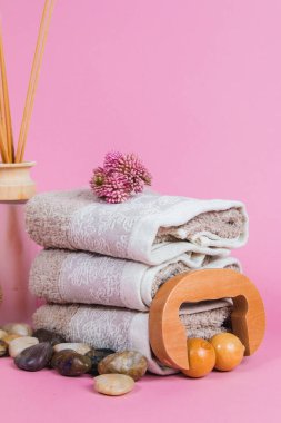 Spa malzemeleri, aroma çubukları taşlar, havlular ve pembe arka planda bir bitki.