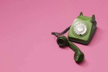 Telsiz ahizesi kaldırılmış ve pastel pembe bir zemin üzerinde oturan eski model yeşil döner telefon. Fotokopi alanı ve sağ tarafta kompozisyonu olan metin için yer var..