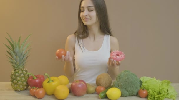 Meisje met een slanke figuur die een donut en tomaat vasthoudt — Stockvideo