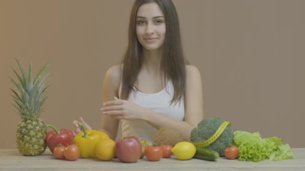 Девушка улыбается в камеру и показывает овощи и фрукты — стоковое видео