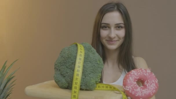 Beautiful girl brings broccoli and gingerbread to camera — Stock Video