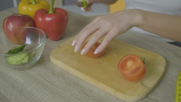 Девушка садится за стол и режет помидор. — стоковое видео