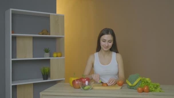 Кавказская девушка смотрит на стол и режет помидоры — стоковое видео