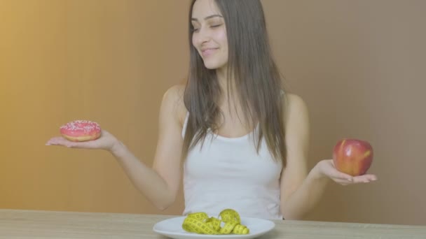 Mädchen mit schlanker Figur hält einen Donut und einen Apfel in der Hand — Stockvideo